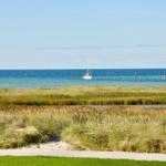 Sailboat auf dem Meer vor Strand mit Gras und Pfad.