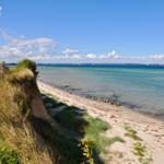 Strand mit Klippe und klarer See unter blauem Himmel mit Wolken.