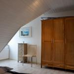 Schlafzimmer mit Holzschrank, Stuhl und Bild an der Wand unter schrägem Dach.