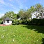 Ein weißer Pavillon mit dunklem Dach steht auf einer grünen Wiese mit weißen Blumen.