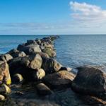 Steinreihe führt ins Meer unter blauem Himmel