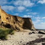 Steilküste mit Strand und Felsen unter blauem Himmel.