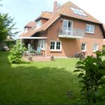 Rotes Backsteingebäude mit Balkon und Garten. Terrasse mit Stühlen und Pflanzen.