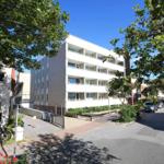 Wohnhaus mit Balkonen, umgeben von Bäumen und gepflasterten Wegen.