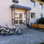 Eine weiße Motorrad steht vor der Eingangstür eines Hauses mit gepflastertem Hof.