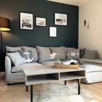 Ein Wohnzimmer mit grauem Sofa, Holztisch und dunkler Wand