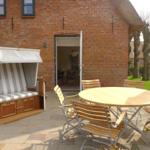 Terrasse mit Strandkorb und runden Tisch mit Stühlen vor Backsteinhaus