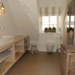 Badezimmer mit Waschbecken, Toilette und Dusche. Holzregal, Spiegel und Fenster mit Vorhang.