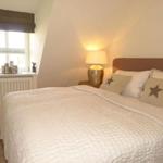 Schlafzimmer mit Bett, Nachttisch, Lampe und Fenster.