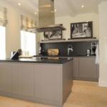 Moderne Küche mit Kücheninsel, dunkler Arbeitsplatte und Fenstern mit Raffstoren.