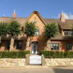 Rotes Backsteinhaus mit Strohdach, grünen Bäumen und weißem Tor