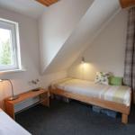 Zimmer mit zwei Betten, Fenstern und Dachschräge.