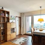 Esszimmer mit Tisch, Stühlen und Blick auf Balkon. Holzregal mit Büchern und Glasvitrine.