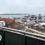 Blick vom Balkon auf Hafen, Parkplatz und Wasser mit Schneeflächen.