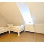 Zimmer mit zwei Betten, Dachschräge und Holzboden. Weiße Möbel und Heizung.