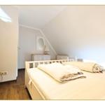 Schlafzimmer mit Dachschräge, Bett, Kleiderschrank und Spiegel.