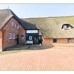 Haus mit Strohdach und Backsteinfassade, Vorgarten mit Steinplatten und weiße Bank.