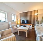 Wohnzimmer mit Sofa, Sessel, Tisch und Fernseher. Wand mit Streifenmuster.