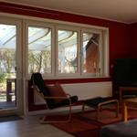 Wohnzimmer mit roten Wänden, Sitzgelegenheit und TV. Blick auf Terrasse und Garten.