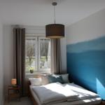 Schlafzimmer mit Holzbett, Fenster und blauer Wand. Hängelampe und Nachttisch.