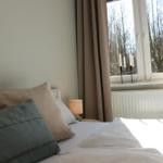 Ein Bett mit Kissen und einer Lampe neben einem Fenster mit Vorhängen.