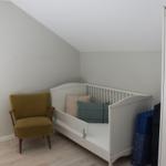 Kinderzimmer mit weißem Bett, gelber Sitzgelegenheit und Holzboden.