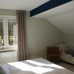 Schlafzimmer mit Bett, Kinderbett und Fenster. Dachgeschoss mit Holzboden und dunkler Deckenleiste.
