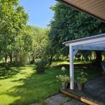 Terrasse mit Sitzgelegenheiten und Pflanzen. Hintergrund: grüner Garten mit Bäumen und Feuerkorb.