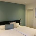 Schlafzimmer mit Doppelbett, grüner Wand und Nachttischbeleuchtung.