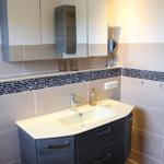 Badezimmer mit Waschtisch, Spiegelschrank und Fliesenverkleidung.