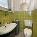 Badezimmer mit grünen Fliesen, Waschbecken, Toilette und Spiegel.