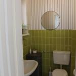 Badezimmer mit Toilette, Waschbecken und Spiegel an gestreifter Wand.