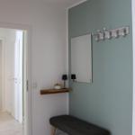 Eingangsbereich mit Bank, Wandgarderobe und Spiegel an mintfarbener Wand.