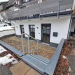 Moderne Wohnung mit Balkon, Eingangstreppe und Gartenbereich. Schnee liegt im Vorgarten.