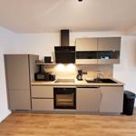 Küche mit Dunstabzug, Spüle und Backofen. Holzfußboden und Wanduhr sichtbar.