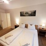 Schlafzimmer mit Doppelbett, zwei Nachttischen und Wandbild. Holzboden und angrenzender Badraum.