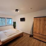 Schlafzimmer mit Bett, Kleiderschrank und Fernseher an der Wand.