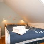 Schlafzimmer mit Dachschrägen, Bett mit Decke und Handtüchern, Nachttisch mit Pflanze und Büchern.