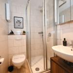 Badezimmer mit Dusche, Waschbecken und Toilette. Weiße Fliesen und Holzunterschrank.