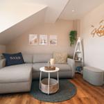 Wohnzimmer mit grauem Sofa, runden Tisch und Holzboden unter schrägen Dach