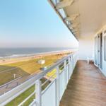 Terrasse mit Meerblick, Holzboden und weißer Brüstung. Blick auf Strand und Grünfläche.