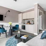 Wohnbereich mit Küche, Sofa und Esstisch. Blaue Stühle und Fernseher an der Wand.