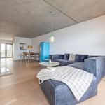 Wohnzimmer mit Sofa, Couchtisch und blauem Kühlschrank. Holzboden und Betondecke.