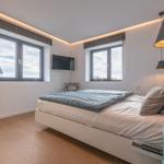 Schlafzimmer mit Bett, Fenstern und TV. Holzboden und gelber Schrank.
