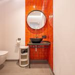 Badezimmer mit orangefarbenen Fliesen, runden Spiegel und schwarzem Waschbecken.