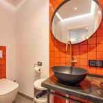 Badezimmer mit orangefarbenen Fliesen, runden Spiegel und schwarzer Waschschale.