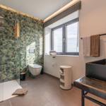 Badezimmer mit Dusche, Toilette und Waschbecken. Fenster mit Blick auf Meer.
