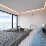 Schlafzimmer mit großem Fenster und Meerblick. Bett mit Kissen und Handtuchschwanen.