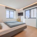 Schlafzimmer mit Bett, Fenstern, Kleiderschrank und Deckenleuchte.