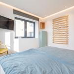 Schlafzimmer mit Bett, Fenster, TV und Kleiderständer.